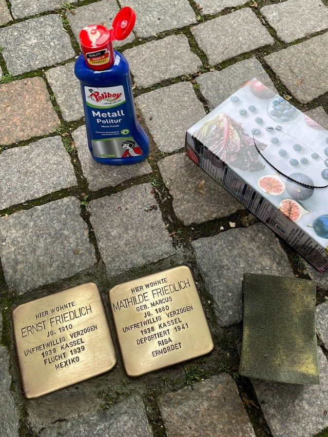 Zwei gereinigte Stolpersteine in der Bünder Innenstadt erinnern an Ernst und Mathilde Friedlich. Daneben liegen Metallpolitur und weitere Reinigungsutensilien, die bei der Pflege der Gedenksteine verwendet wurden.