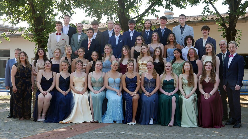 Die Abiturient:innen des Jahrgangs 2026 der Gesamtschule Rödinghausen stehen gemeinsam mit Schulleitung und Oberstufenteam für das offizielle Abschlussfoto auf dem Schulgelände. Die Schüler:innen tragen festliche Kleidung anlässlich ihrer Abiturfeier.