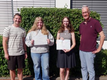 Zwei Schülerinnen präsentieren gemeinsam mit Französischlehrer Matthias Janoschka und Schulleiter Andreas Hillebrand ihre DELF-Diplome. Die Auszeichnungen bescheinigen erfolgreich erworbene Französischkenntnisse auf unterschiedlichen Niveaustufen.