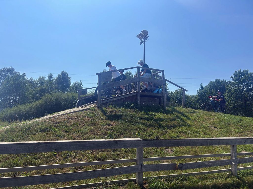 Mehrere Schüler:innen warten mit ihren Mountainbikes auf der Startrampe eines Pumptracks auf ihren nächsten Durchgang. Beim gemeinsamen Training sammeln sie Erfahrungen im sicheren Fahren auf anspruchsvollem Gelände.