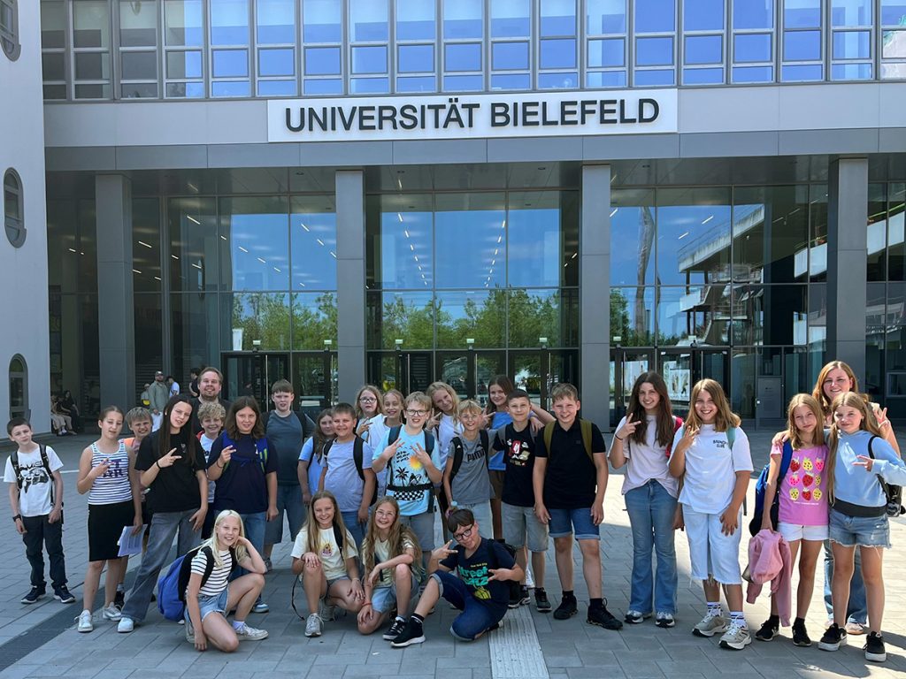 Die Klasse 5d steht gemeinsam mit ihrer Lehrkraft vor dem Haupteingang der Universität Bielefeld. Neben dem Besuch des Teutolab Mathematik erhielten die Schülerinnen und Schüler auch eine Führung über den Campus.
