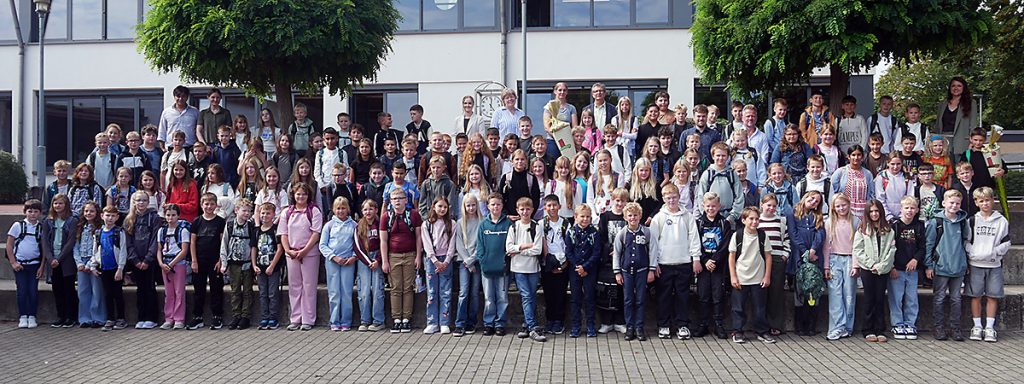 Die neuen Fünftklässler:innen der Gesamtschule Rödinghausen stehen gemeinsam mit ihren Klassenleitungen und weiteren Beteiligten zum Gruppenfoto auf dem Schulhof.