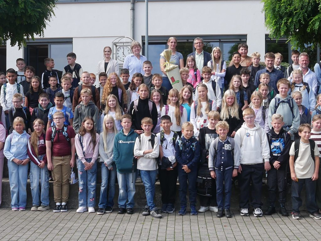 Die neuen Fünftklässler:innen der Gesamtschule Rödinghausen stehen gemeinsam mit ihren Klassenleitungen und weiteren Beteiligten zum Gruppenfoto auf dem Schulhof.