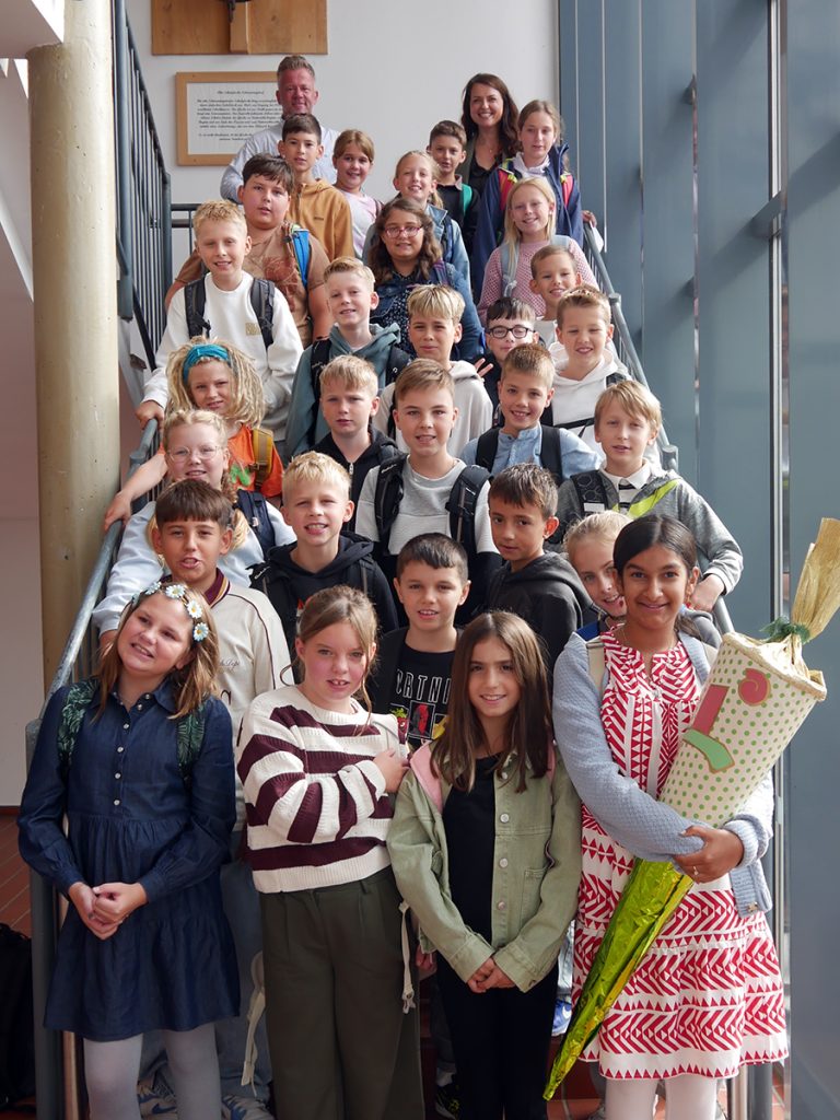 Die Schüler:innen der Klasse 5a stehen nach ihrer Einschulungsfeier gemeinsam mit ihrer Klassenleitung auf einer Treppe in der Gesamtschule Rödinghausen.
