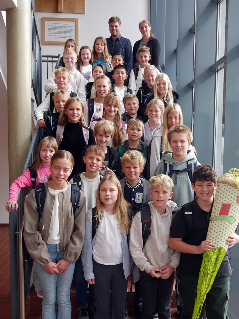 Die Schüler:innen der Klasse 5b stehen nach ihrer Einschulungsfeier gemeinsam mit ihrer Klassenleitung auf einer Treppe in der Gesamtschule Rödinghausen.