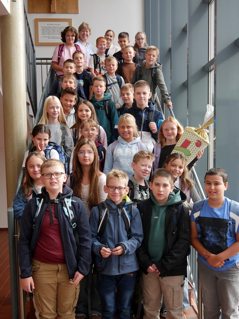 Die Schüler:innen der Klasse 5c stehen nach ihrer Einschulungsfeier gemeinsam mit ihrer Klassenleitung auf einer Treppe in der Gesamtschule Rödinghausen.